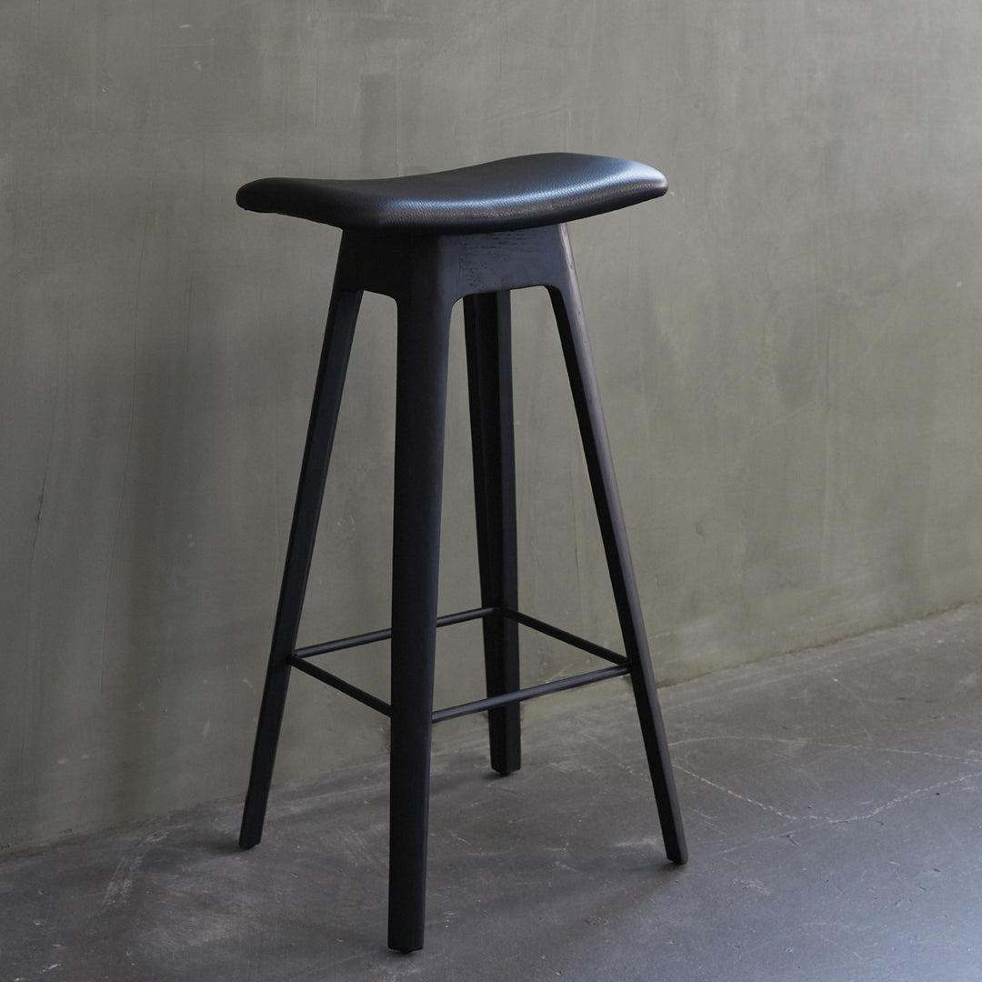 Black wooden bar stool with a sleek, minimal design and a smooth, curved seat against a textured gray background.