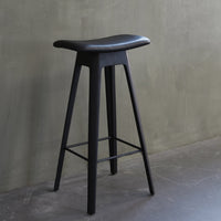 Black wooden bar stool with a sleek, minimal design and a smooth, curved seat against a textured gray background.