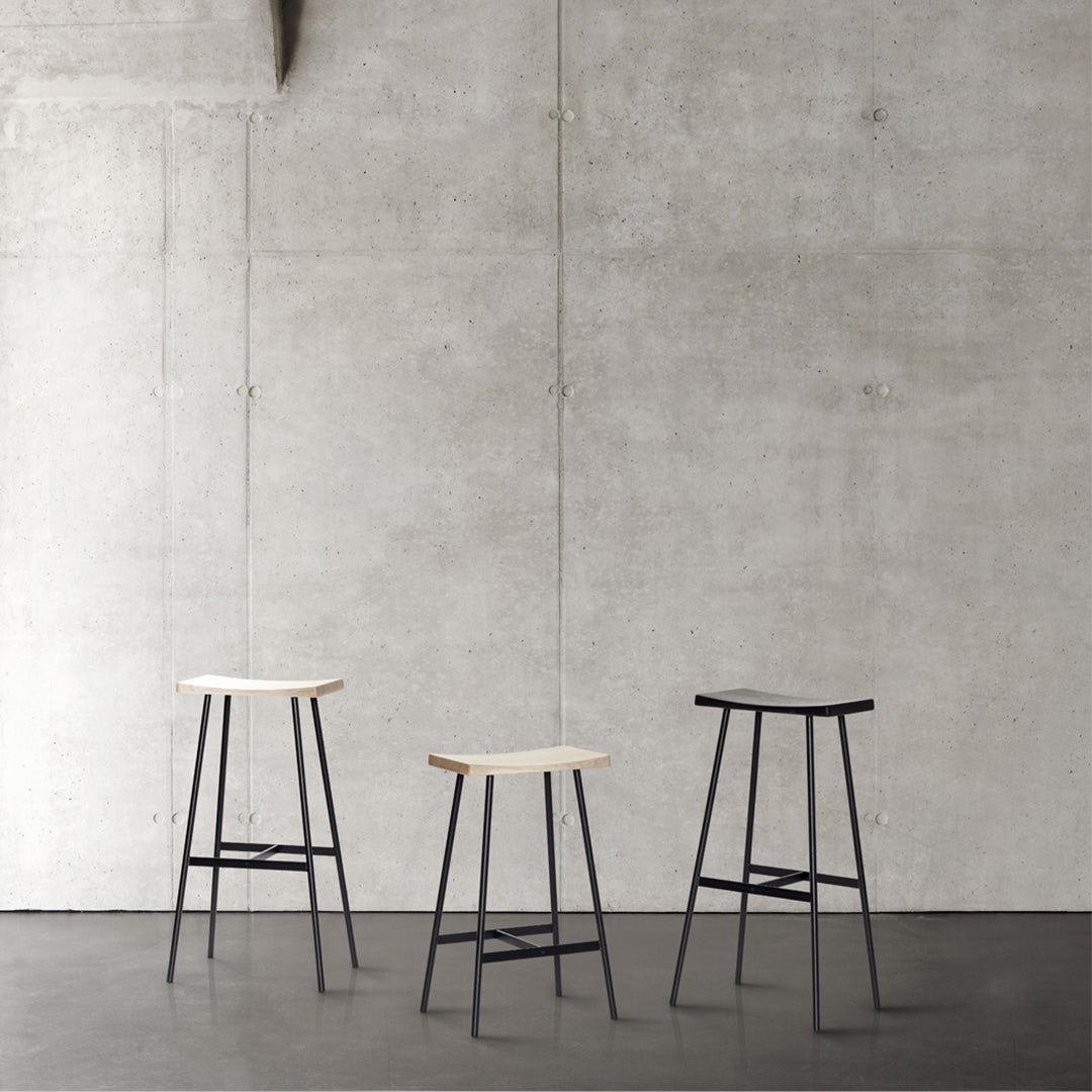 Three modern bar stools with natural wood tops and sleek black metal frames against a minimalist grey backdrop.