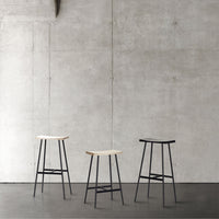 Three modern bar stools with natural wood tops and sleek black metal frames against a minimalist grey backdrop.