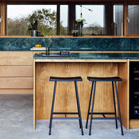"Dark wood bar stools with sleek black frames against a textured green marble countertop."