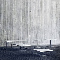 Minimalist white-top tables with sleek chrome frames against a textured concrete background.