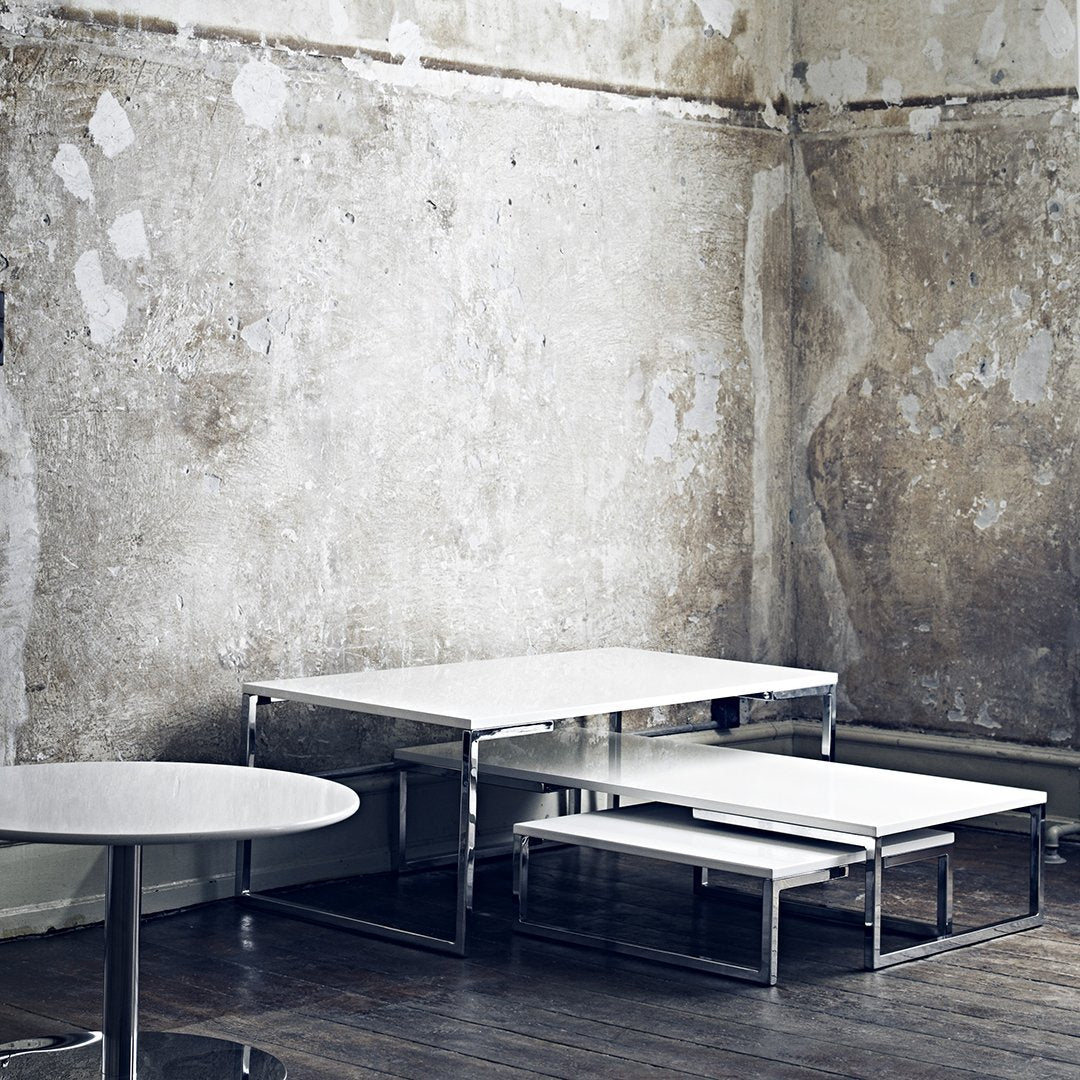 Sleek white tables with chrome accents against a textured gray wall, featuring minimalistic modern design.