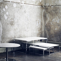 Sleek white tables with chrome accents against a textured gray wall, featuring minimalistic modern design.