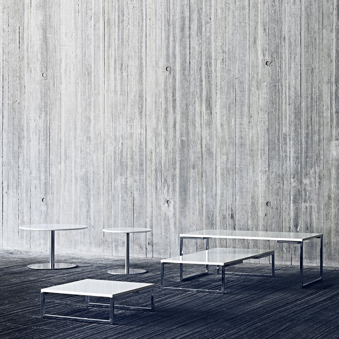 Modern minimalist tables in sleek white with geometric patterns against a textured gray wall.