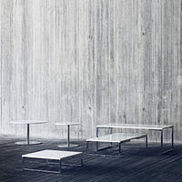 Modern minimalist tables in sleek white with geometric patterns against a textured gray wall.