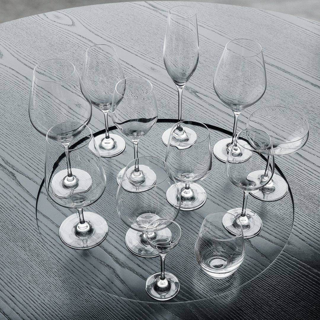 "Set of clear glass wine glasses featuring elegant stem designs on a circular glass platter against a textured grey background."