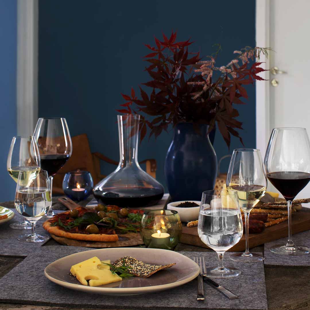 Elegant dining table with gray linens, dark blue vase, clear glassware, rich red leaves, and earthy food tones.