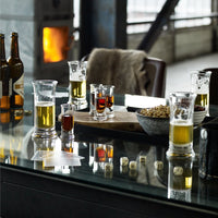 Assorted glasses with golden beers, dark shots, and pops of red, arranged on a rustic table with a reflective surface.