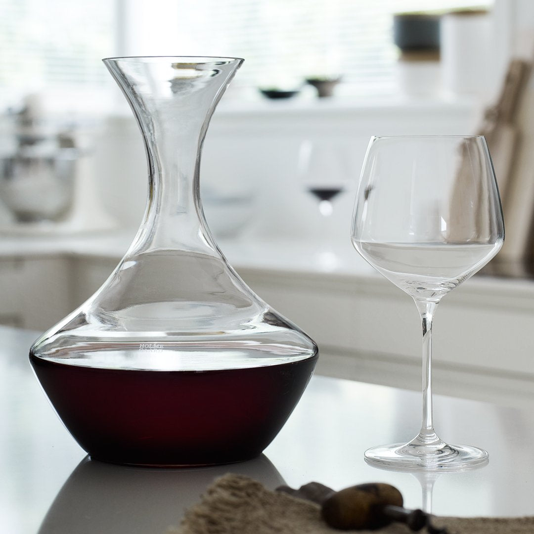 Elegant glass wine decanter with a smooth, clear top and a deep red bottom, paired with a simple clear wine glass.