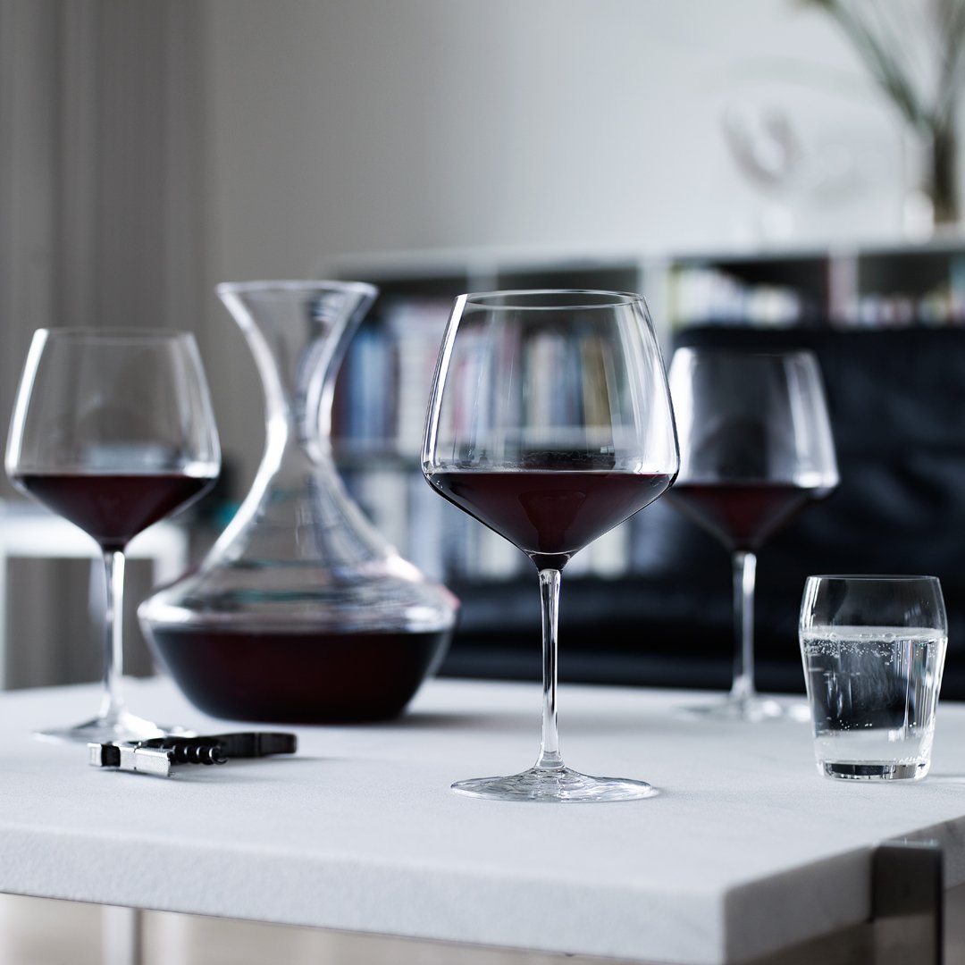 Elegant wine glasses hold deep red wine, paired with a sleek glass carafe, on a minimalist white table.