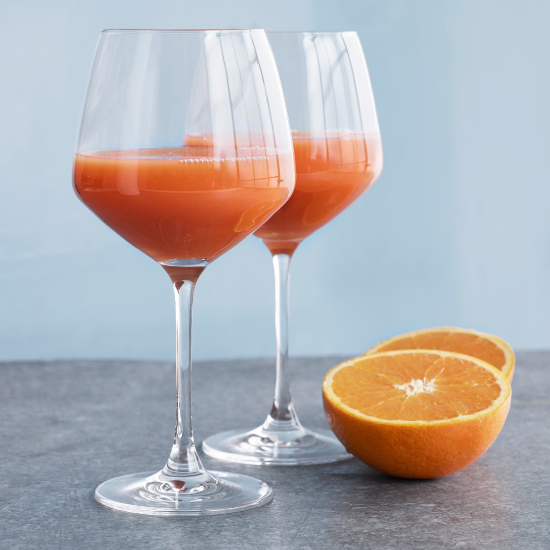 Two clear glasses filled with vibrant orange juice, alongside a halved orange against a light blue background.