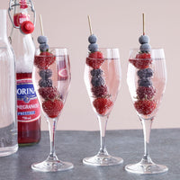 Glasses filled with pink liquid, garnished with vibrant red strawberries and dark blue blueberries on skewers.