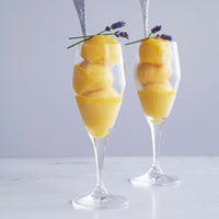 Two clear glasses filled with yellow sorbet, garnished with lavender sprigs, set against a light gray background.