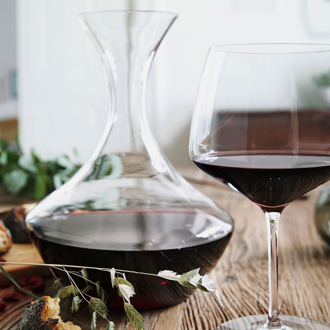 Elegant clear glass decanter and wine glass, featuring rich red wine against a natural wooden backdrop.