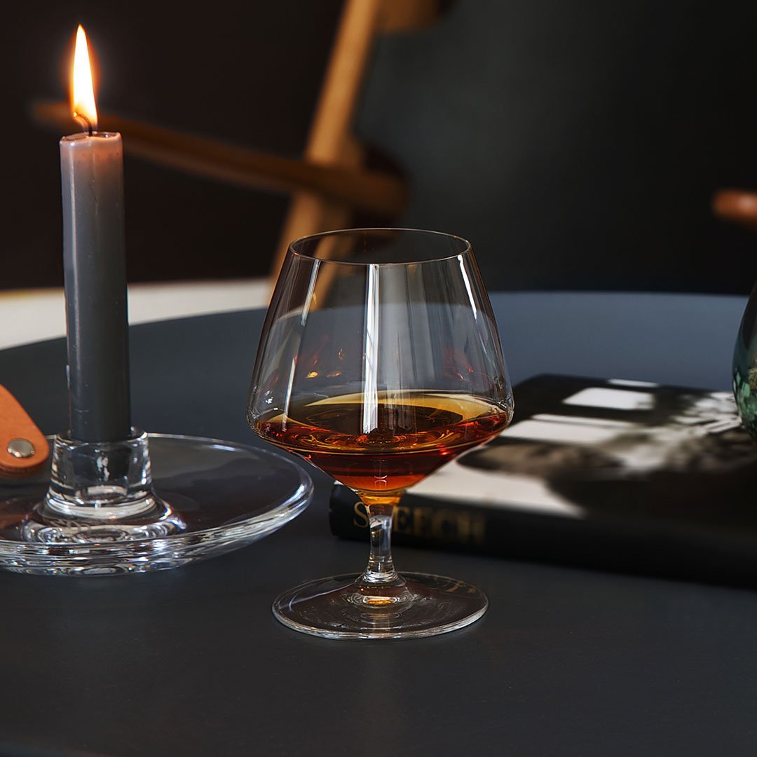 "Elegant crystal glass with amber liquid, set against a dark table and soft gray candlelight."