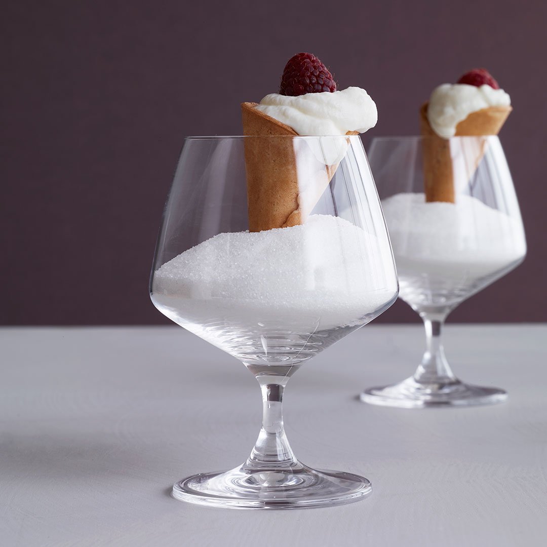 Elegant glass dessert cups with white sugar, topped with creamy frosting and a cone, garnished with raspberries.