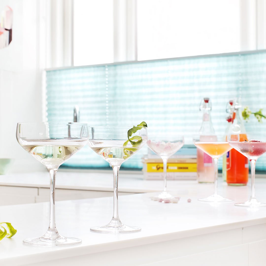 "Elegant glassware with clear, shimmering cocktails set against a vibrant turquoise backsplash."