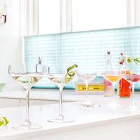 "Elegant glassware with clear, shimmering cocktails set against a vibrant turquoise backsplash."