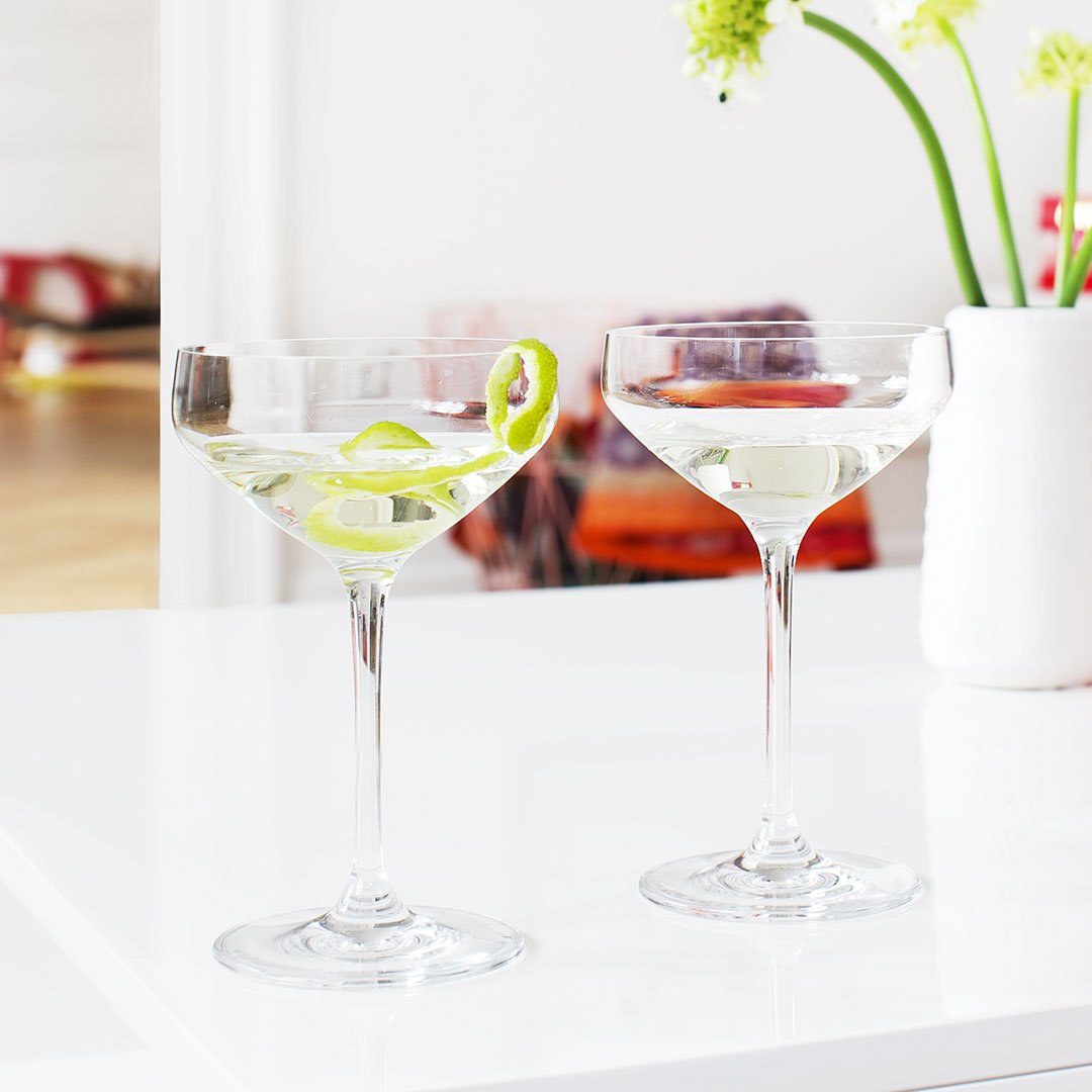 Elegant clear glass martini glasses featuring a fresh lime garnish, set against a bright, minimalist background.