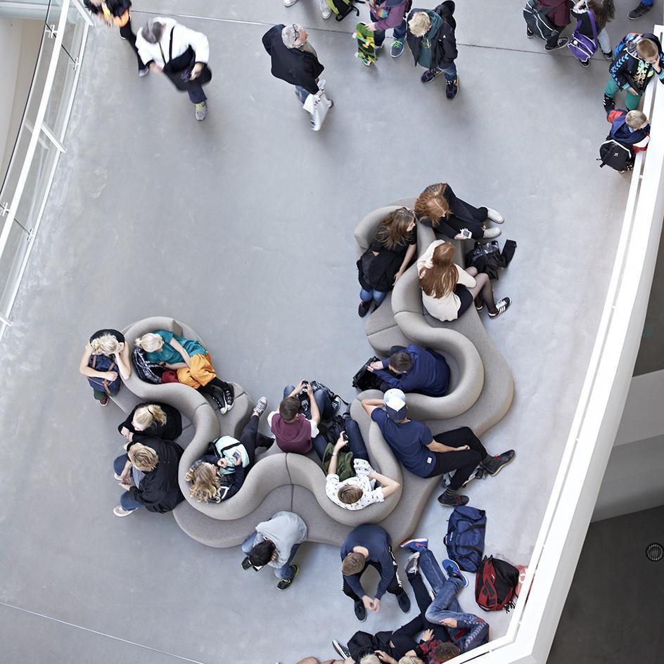 Curved gray seating with soft textures and subtle patterns, surrounded by a diverse crowd in a modern space.