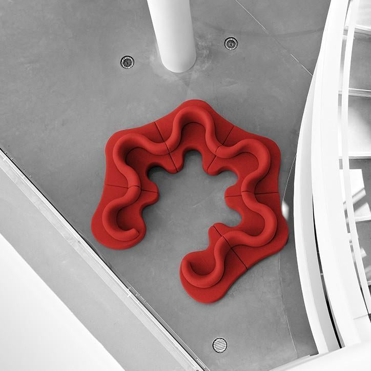 Red abstract wavy sofa with smooth contours, set against a minimalist gray background. Perfect for modern decor.