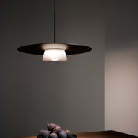 Modern pendant lamp with a sleek black finish and white glass shade, illuminating a minimalist dining space.