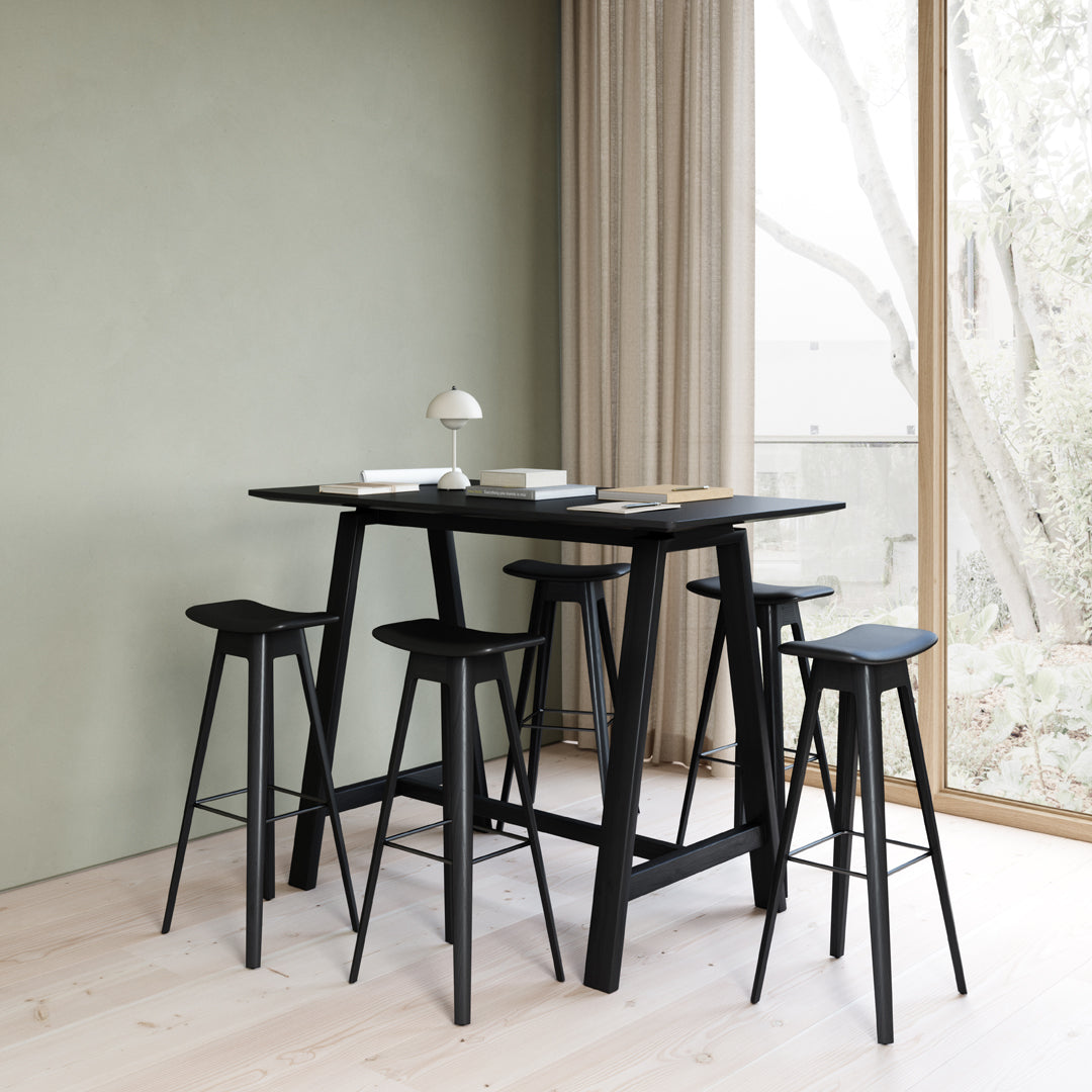 Black bar table and stools against a soft green wall, featuring a minimalist design with sleek lines.
