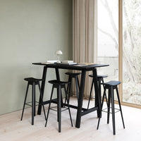 Black bar table and stools against a soft green wall, featuring a minimalist design with sleek lines.
