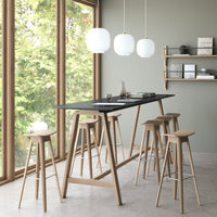 "Stylish black tabletop with natural wood stools, complemented by round white pendant lights and a soft green wall backdrop."