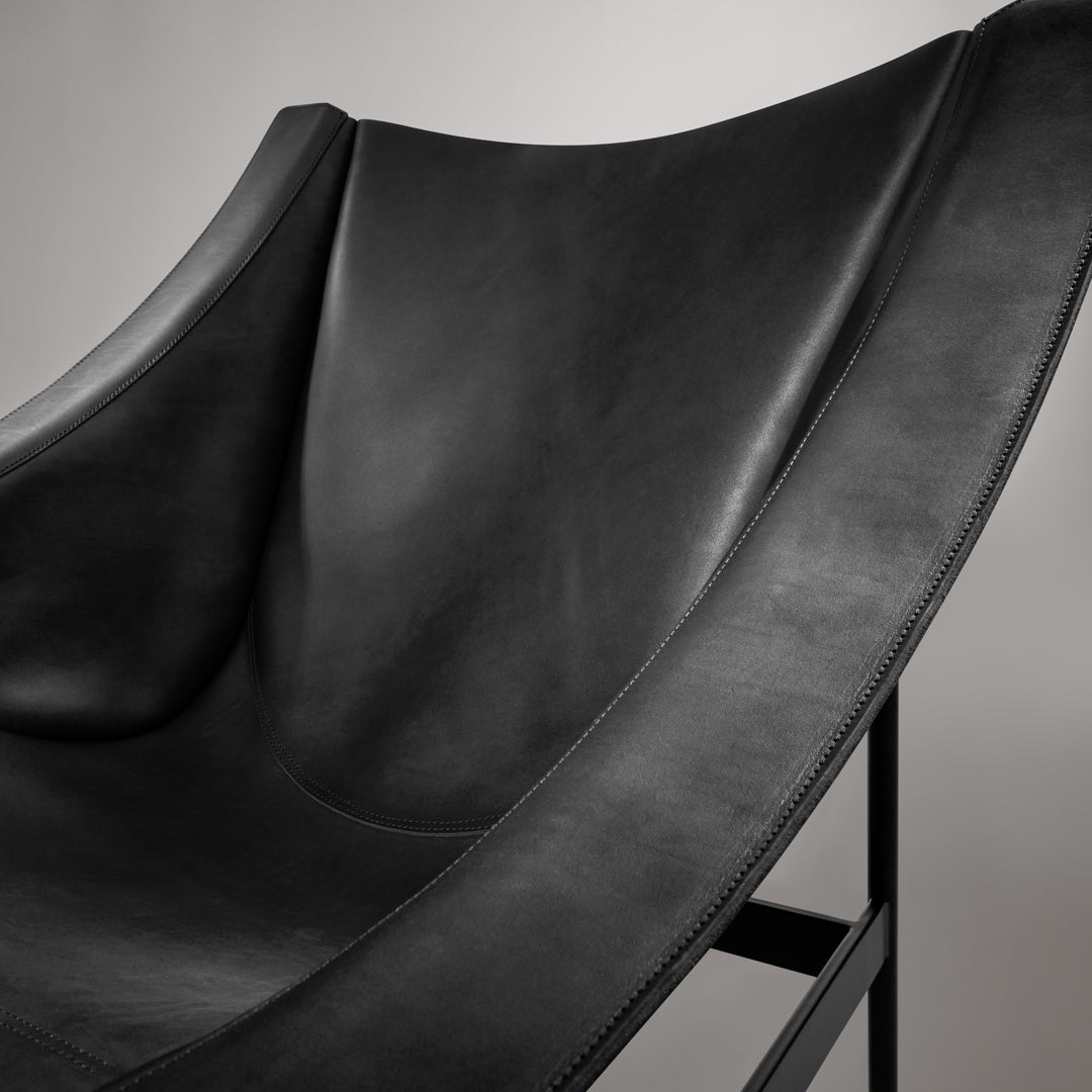 Black leather chair with a smooth, curved design and minimalistic metal frame. Elegant and modern accent piece.