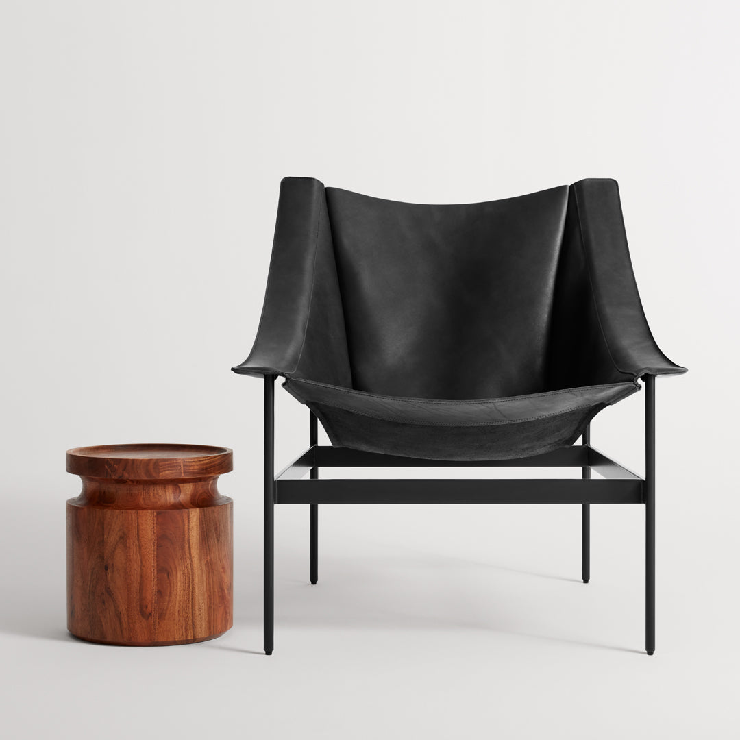 Black leather chair with smooth, curved lines beside a round wooden side table with a rich, warm finish.