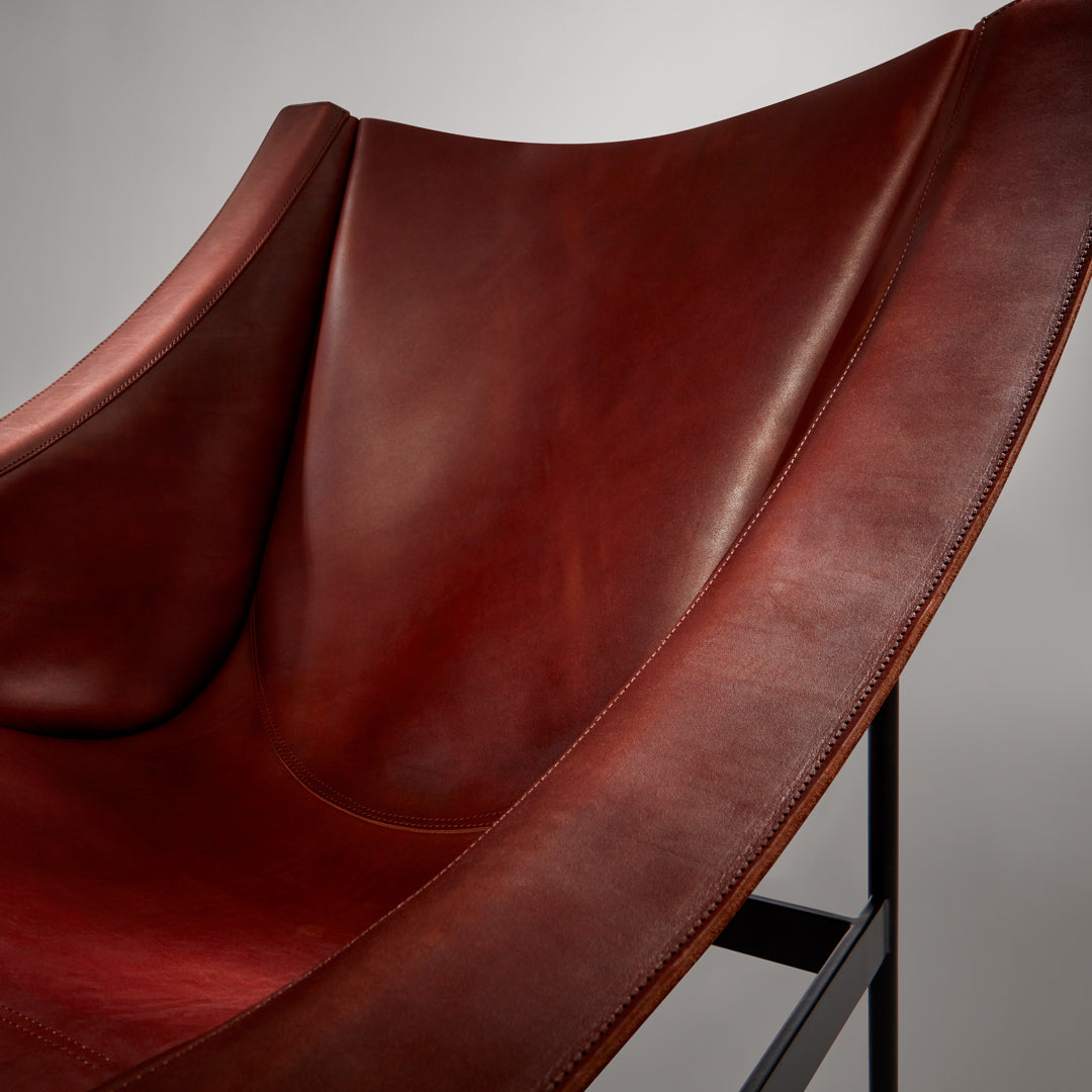 Rich burgundy leather chair with smooth texture and subtle sheen, featuring a minimalist metal frame.