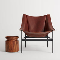 "Brown leather armchair with smooth, minimalist design and a round wooden side table."