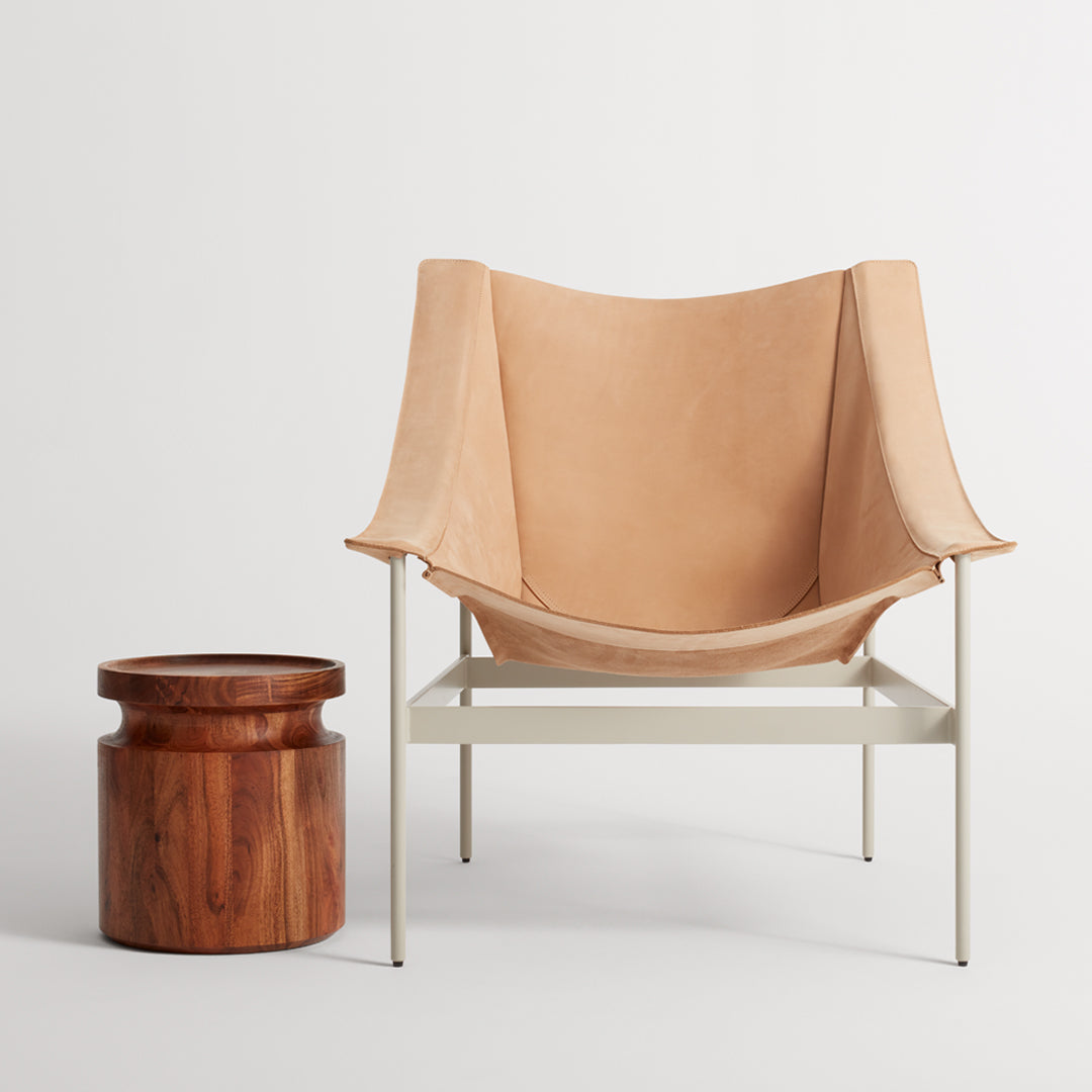 "Light tan fabric chair with minimalist design and a natural wood side table, featuring rich brown tones and smooth textures."