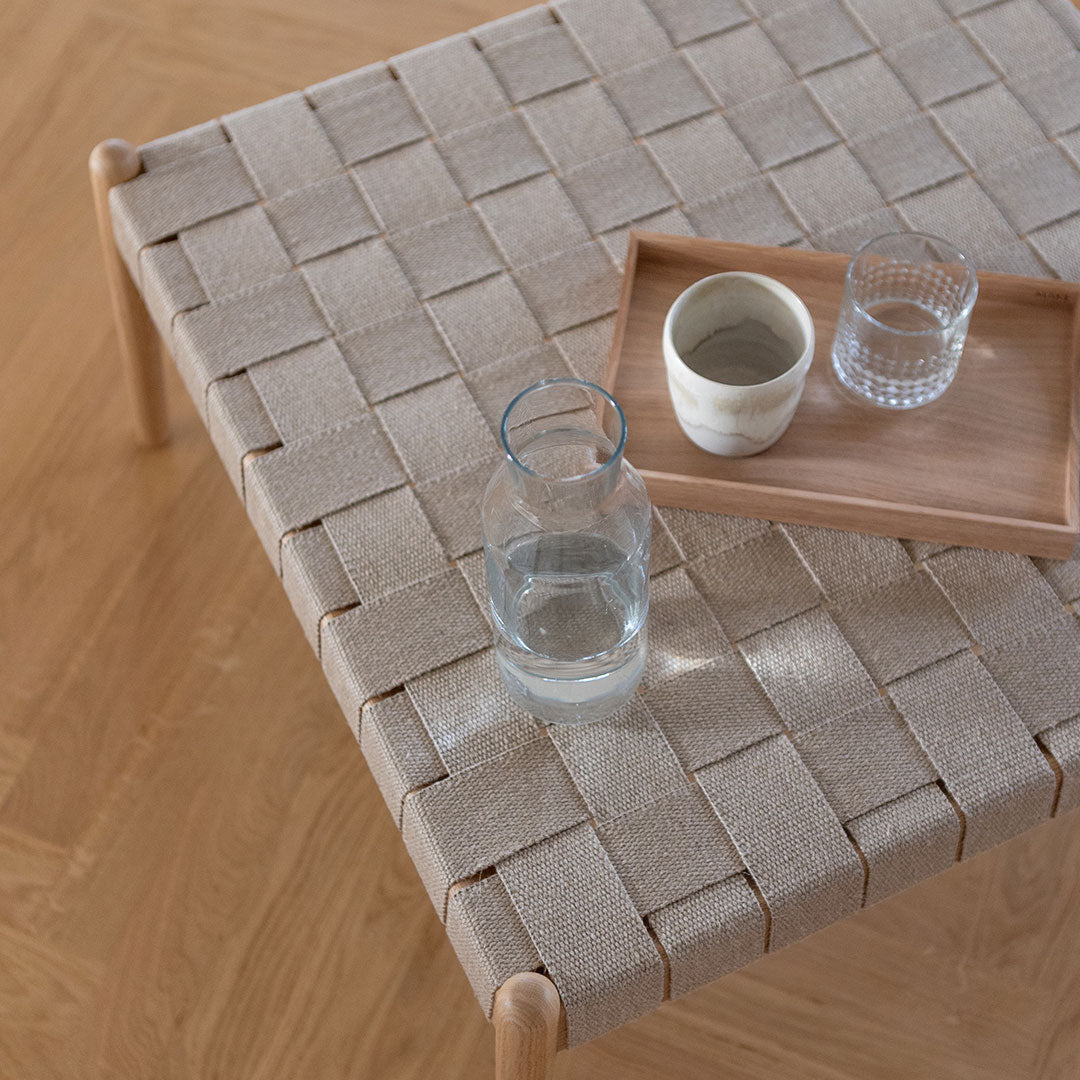 Beige woven table surface with wooden legs, featuring a minimalist design and a natural, textured pattern.