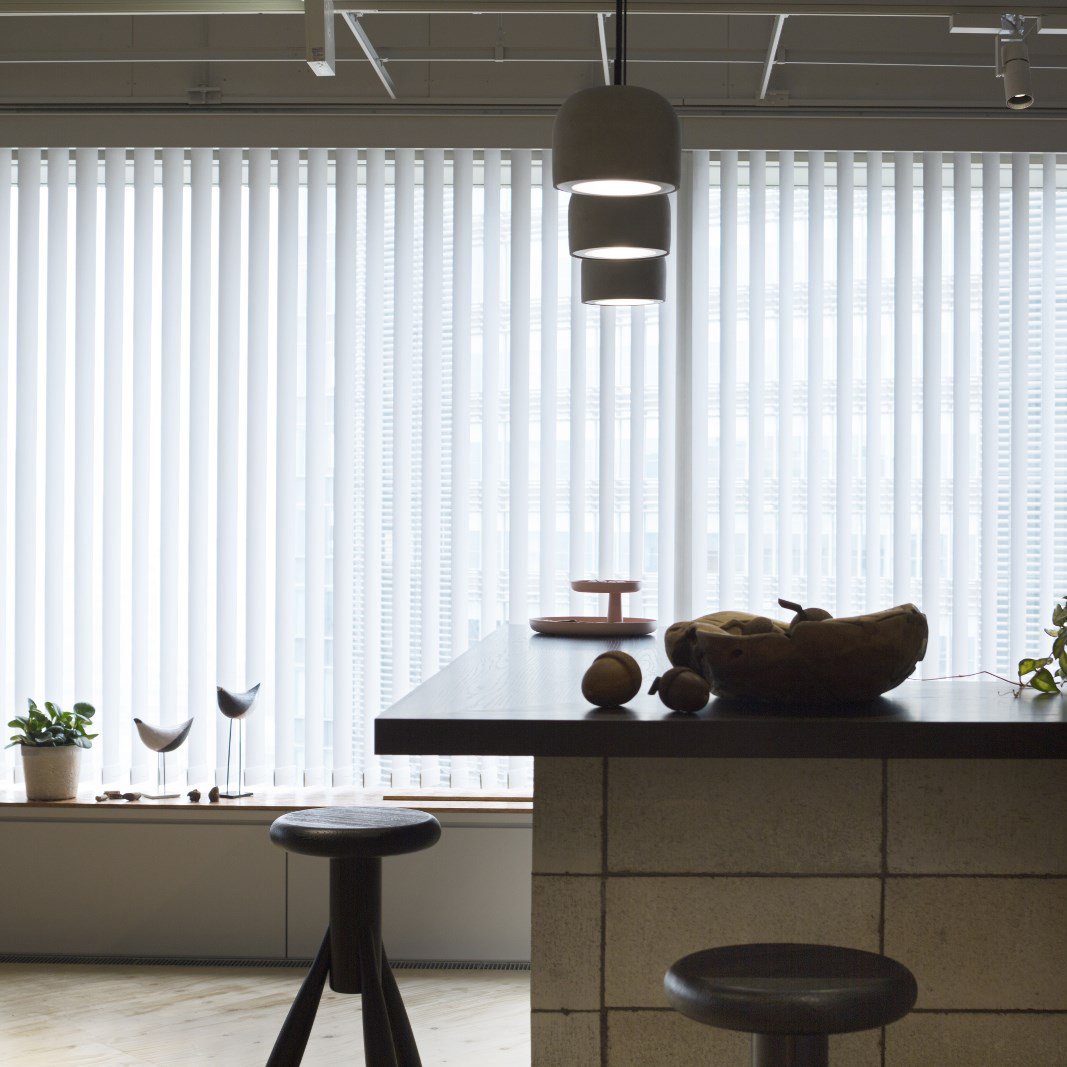 Modern kitchen with white vertical blinds, a dark wood table, and neutral stone accents. Fresh green plants add a pop of color.