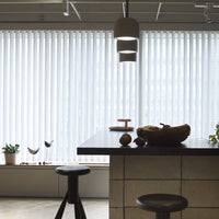 Modern kitchen with white vertical blinds, a dark wood table, and neutral stone accents. Fresh green plants add a pop of color.