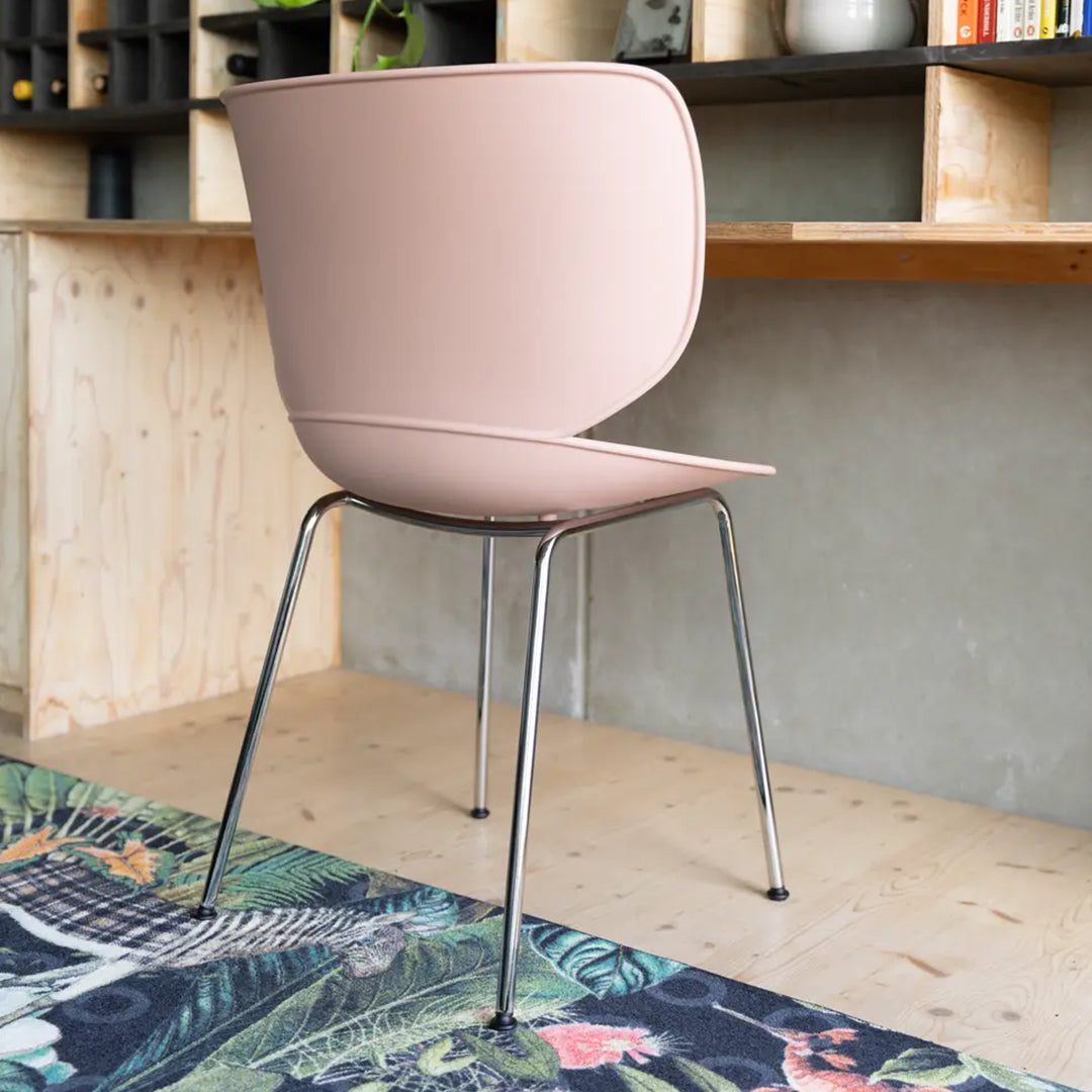 Pink modern chair with sleek chrome legs, positioned on a vibrant tropical-patterned rug.