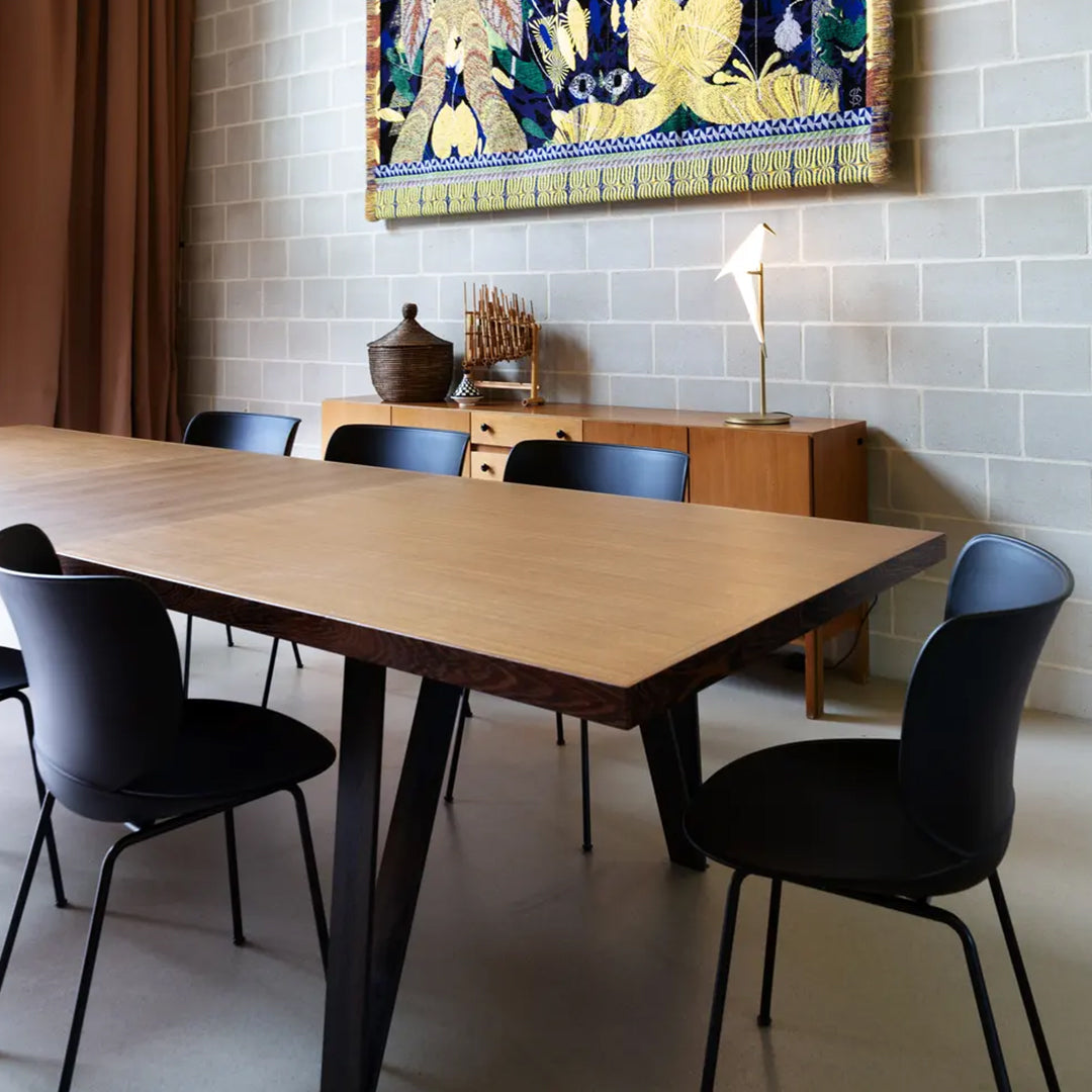 Modern wooden dining table with natural finish, complemented by sleek black chairs in a minimalistic setting.