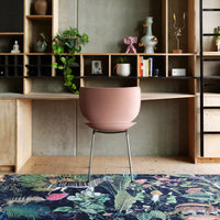 Pink round chair on vibrant floral-patterned rug in a modern interior with wood and concrete accents.