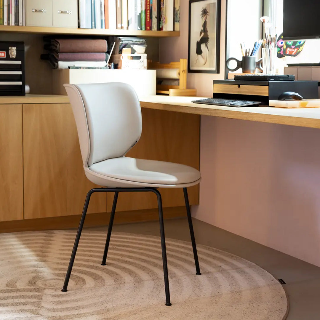 Modern gray chair with a smooth finish and black legs, set against a soft, circular beige rug in a stylish workspace.