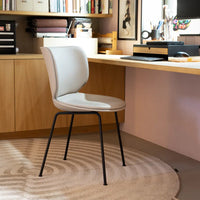Modern beige chair with a smooth finish and black metal legs, set on a circular, softly patterned rug.