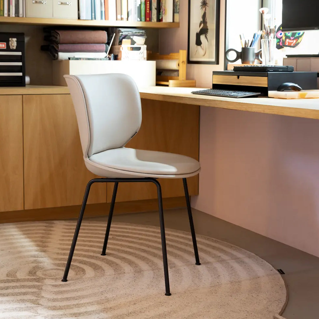 Light gray upholstered chair with a smooth finish and black metal legs, set against a beige circular rug.