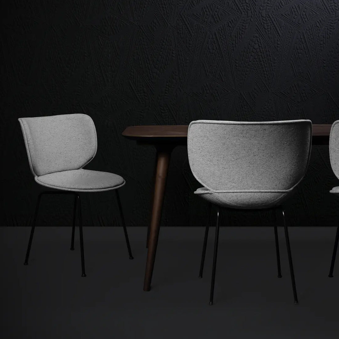 Gray upholstered chairs with smooth curves, set against a dark textured wall and a wooden table.