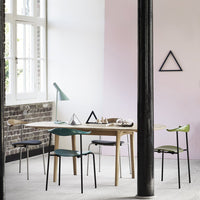 Modern dining space featuring a light wood table, geometric decor, and chairs in green and black tones against pastel walls.