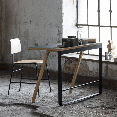 Modern black and natural wood table with minimalist chair, featured against a rustic gray backdrop.