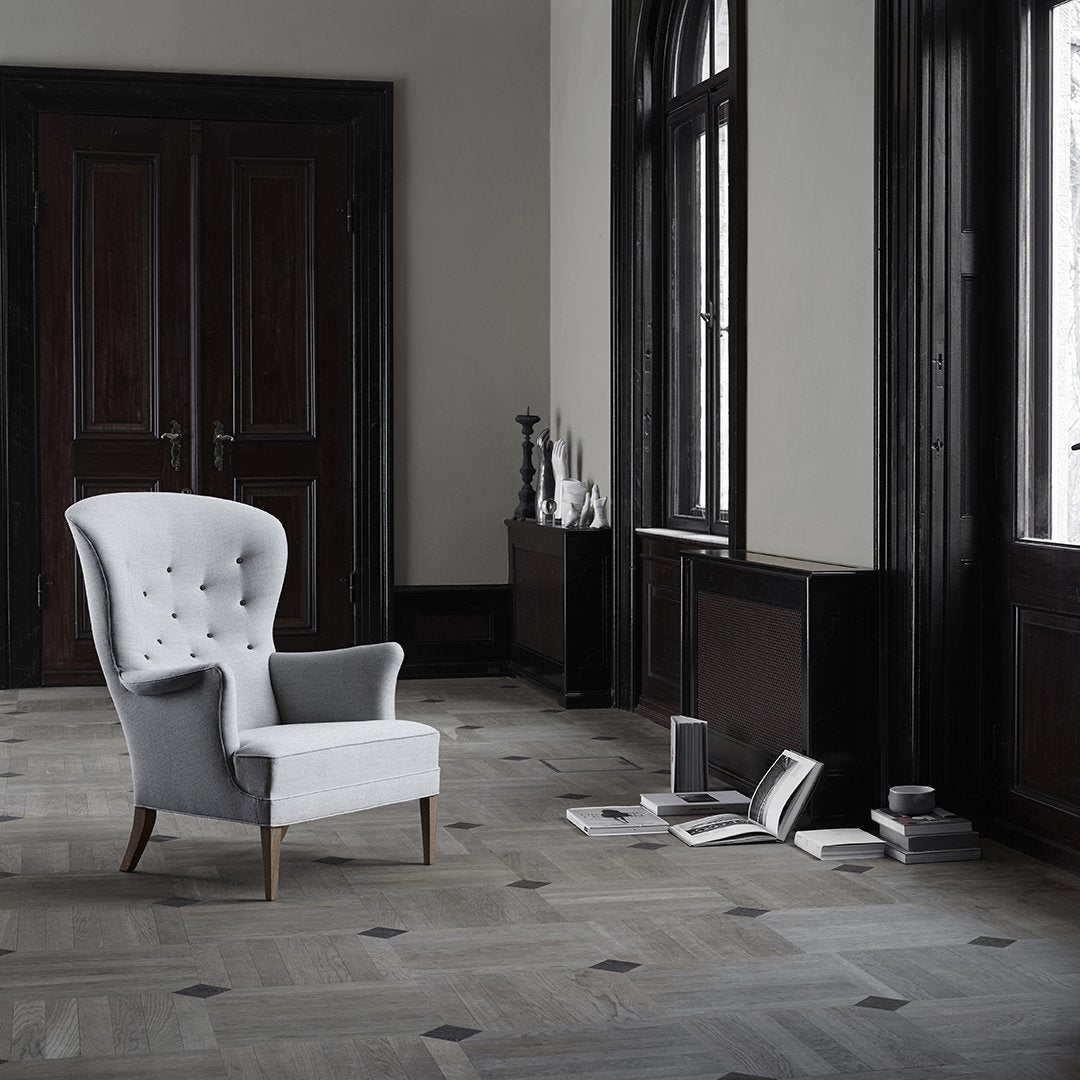 Elegant white upholstered chair with tufted design, set against a muted gray floor and dark wooden accents.