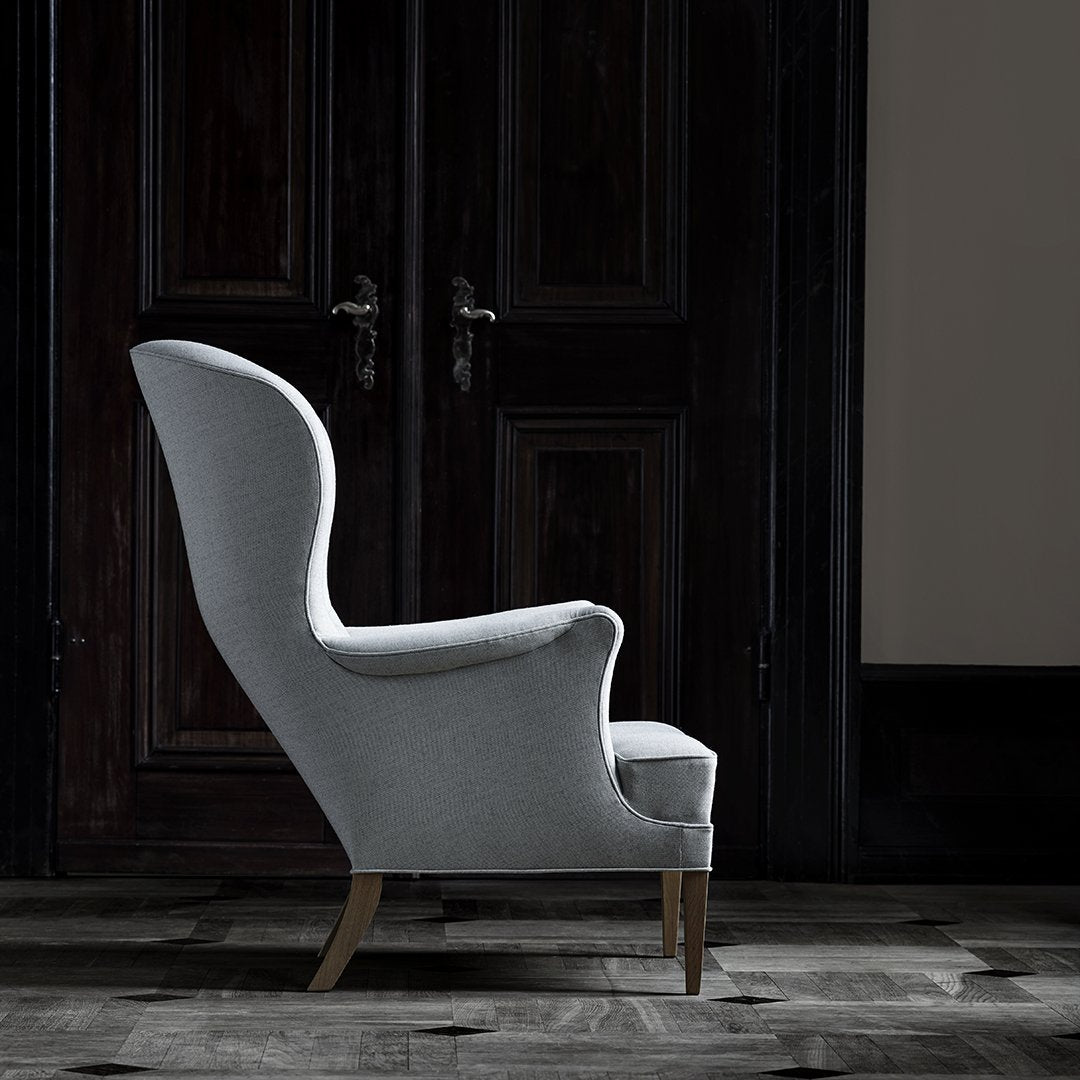 Light gray upholstered chair with a sleek, curved silhouette and wooden legs, set against dark wooden doors.