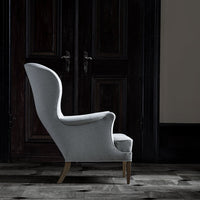 Light gray upholstered chair with a sleek, curved silhouette and wooden legs, set against dark wooden doors.